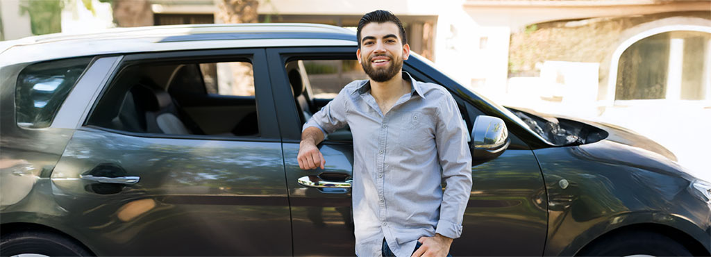 alt="Taxista joven sonriendo junto a su auto, reflejando cómo sacarle más provecho a su trabajo diario gracias a Credimovil."